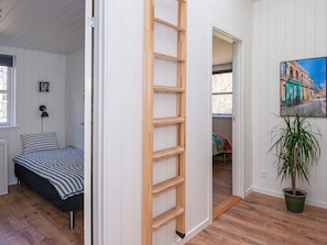 Un dormitorio con cama, escalera de madera, planta en maceta y un cuadro en la pared.