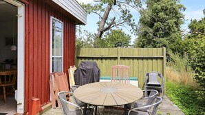 A patio with a round table and metal chairs, a wooden deck, and a red building with a door. - 6 Person Holiday Home in Gorlev (Gørlev)