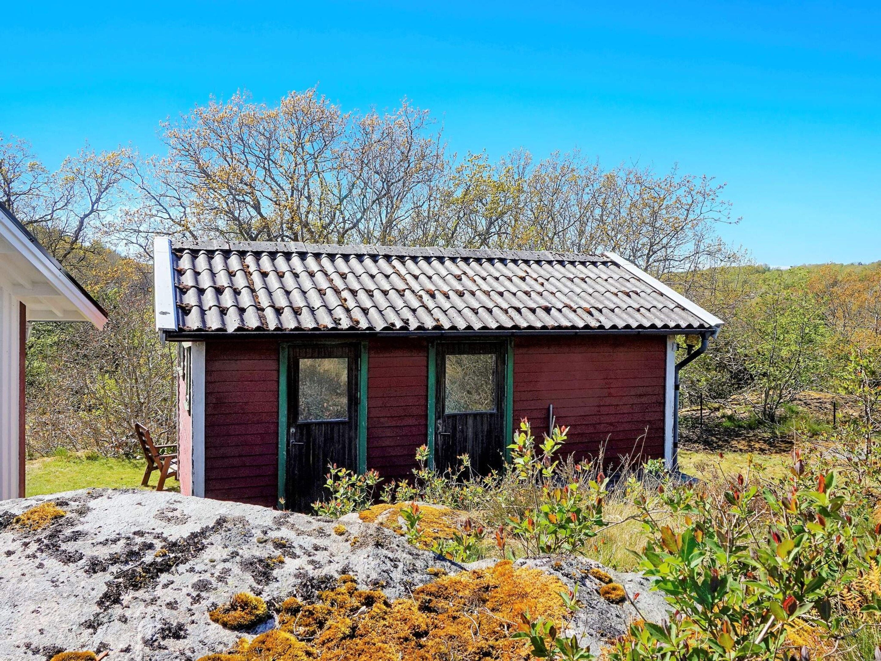 A small, single-story building with a tiled roof and a green door, surrounded by natural vegetation and trees.