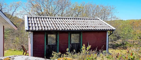 A small, single-story building with a tiled roof and a green door, surrounded by natural vegetation and trees.