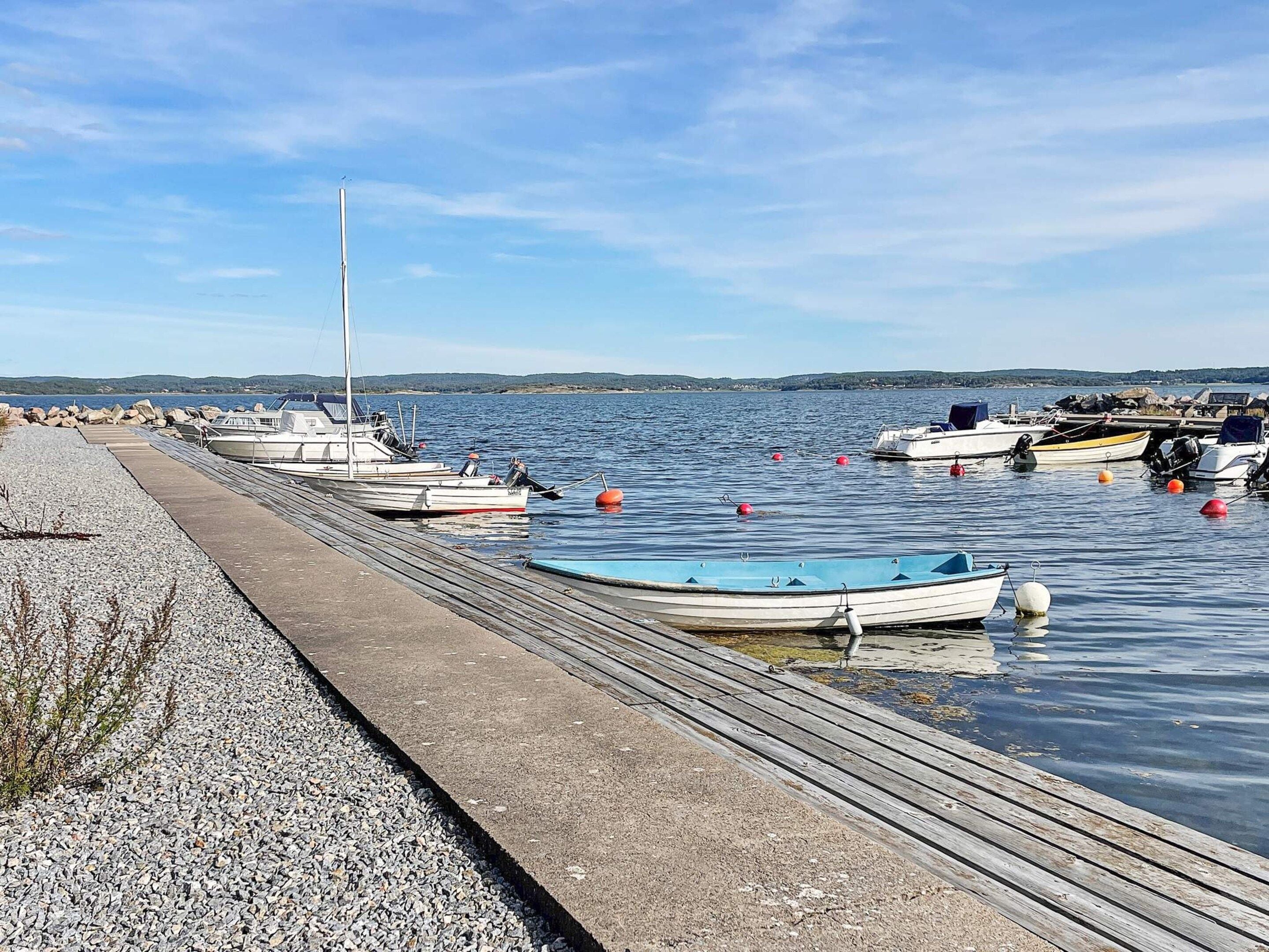 Um cais com barcos atracados, uma praia de pedras e águas calmas.