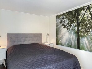 Une chambre à coucher comprenant un lit, une table de chevet, une lampe et une grande fresque murale sur le thème de la forêt.