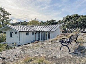 Un petit bâtiment blanc avec un toit en métal, un banc et un chemin de pierres.