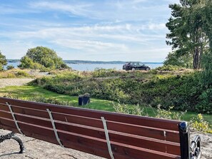 A bench overlooking a grassy area with a car parked in the distance and a body of water in the background. - 7 Person Holiday Home in Hakenaset (Hakenäset)