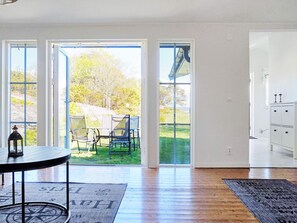 Une pièce avec une table ronde, une lanterne et un tapis orné de motifs. Il y a trois portes qui donnent sur l’extérieur, ainsi qu’un meuble contenant des bougies.