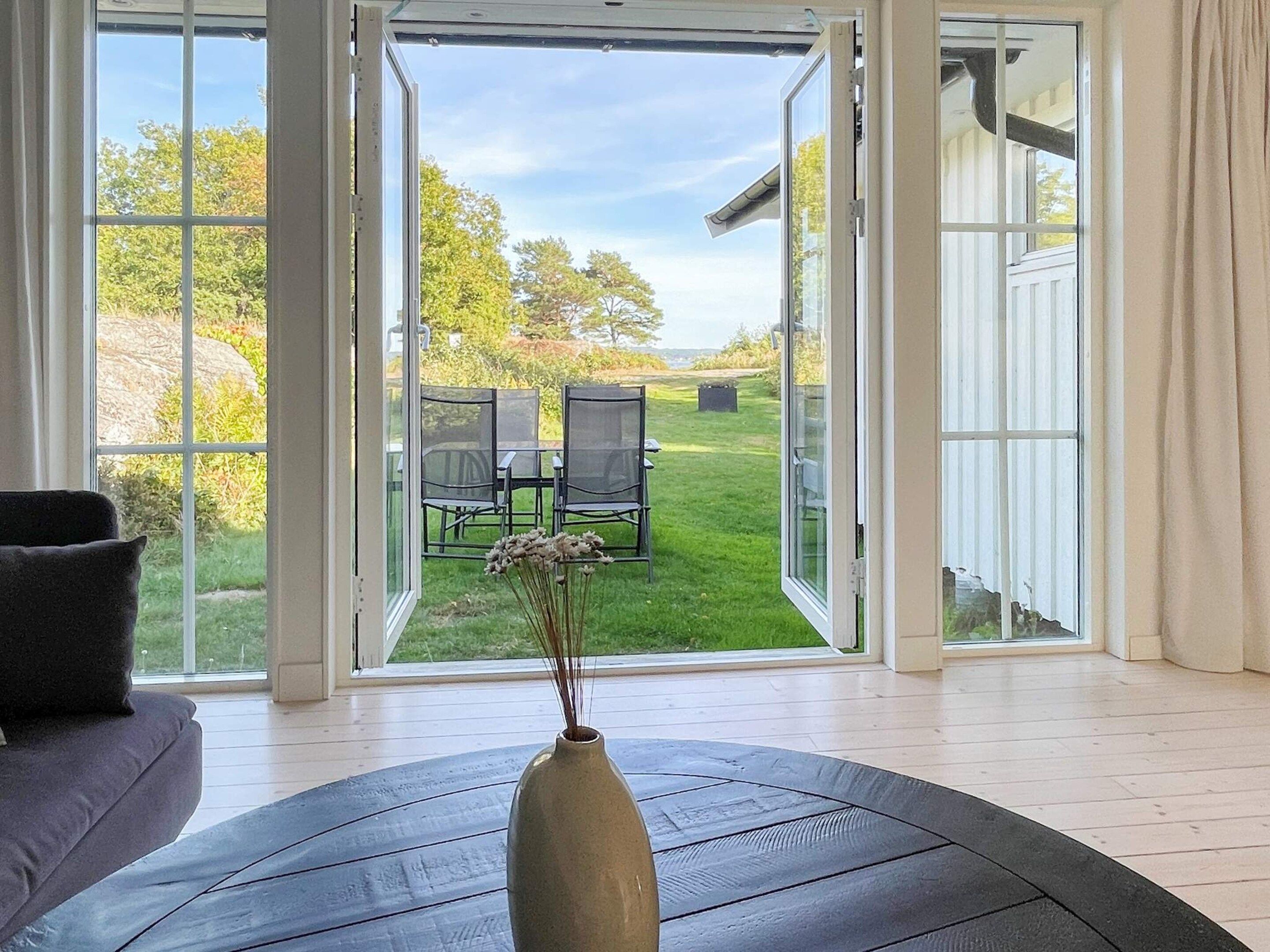 A room with a large glass door leading to an outdoor seating area with chairs and a table.