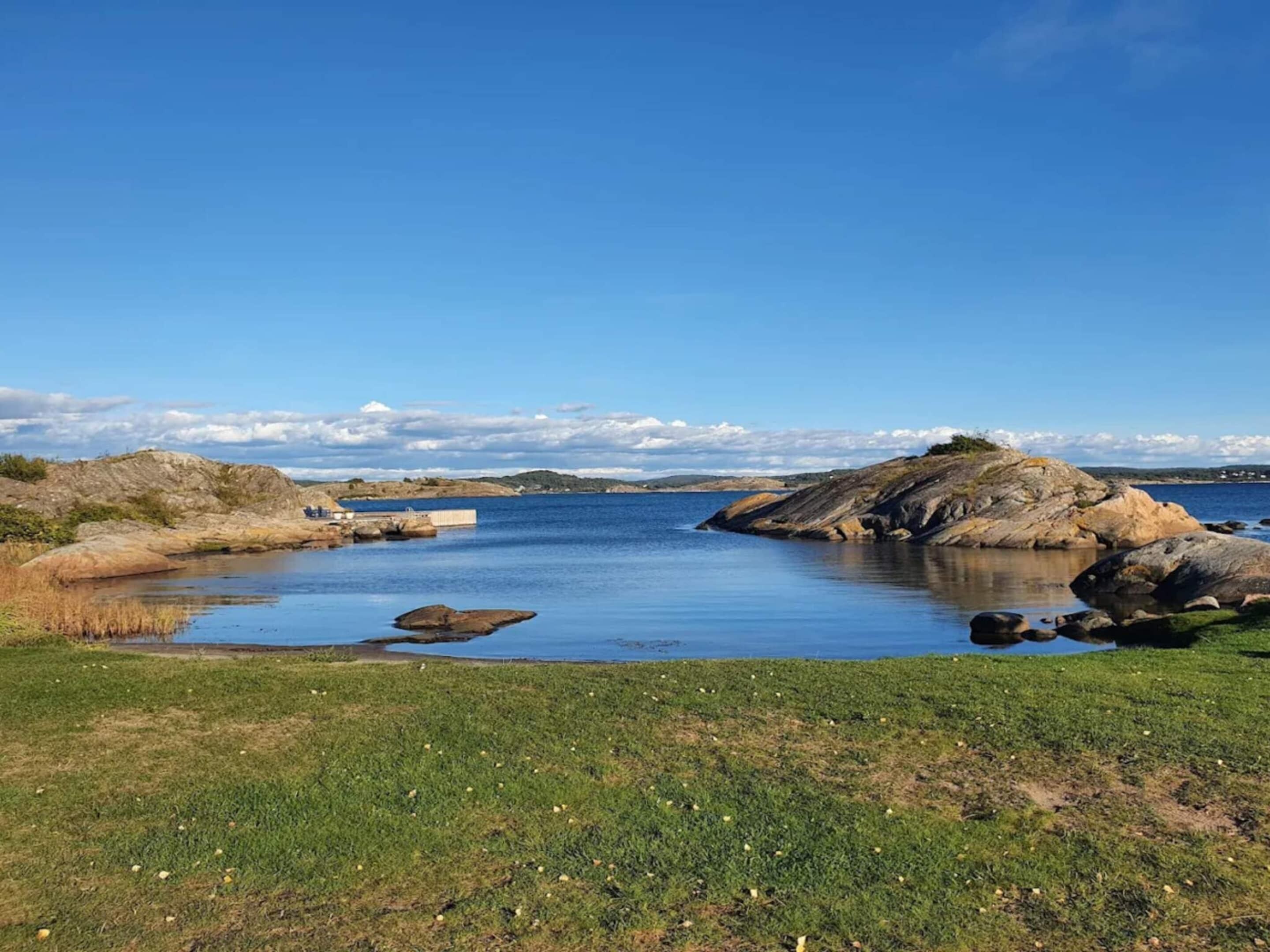 Et kystlandskab med et roligt vandareal, klippeudspring og grønne områder.