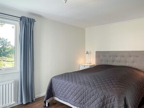 A bedroom with a bed, a nightstand, a lamp, a window with curtains, and a view of greenery outside. - 7 Person Holiday Home in Hakenaset (Hakenäset)