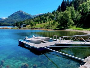 Un lago tranquilo con barcos amarrados a un muelle de madera, rodeado de colinas boscosas.