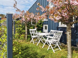 A patio with a table and chairs, surrounded by a garden with flowering trees.