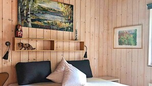 A room with a bed, a wooden headboard, a painting above the bed, a shelf with decorative items, and a lamp. - 5 Star Holiday Home in Bryrup (Bryrup)