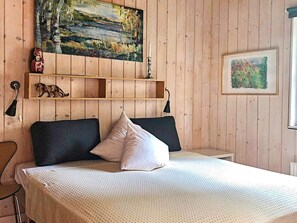 Ein Zimmer mit einem Bett, einem hölzernen Kopfteil, einem Gemälde über dem Bett, einem Regal mit Dekoration und einer Lampe.