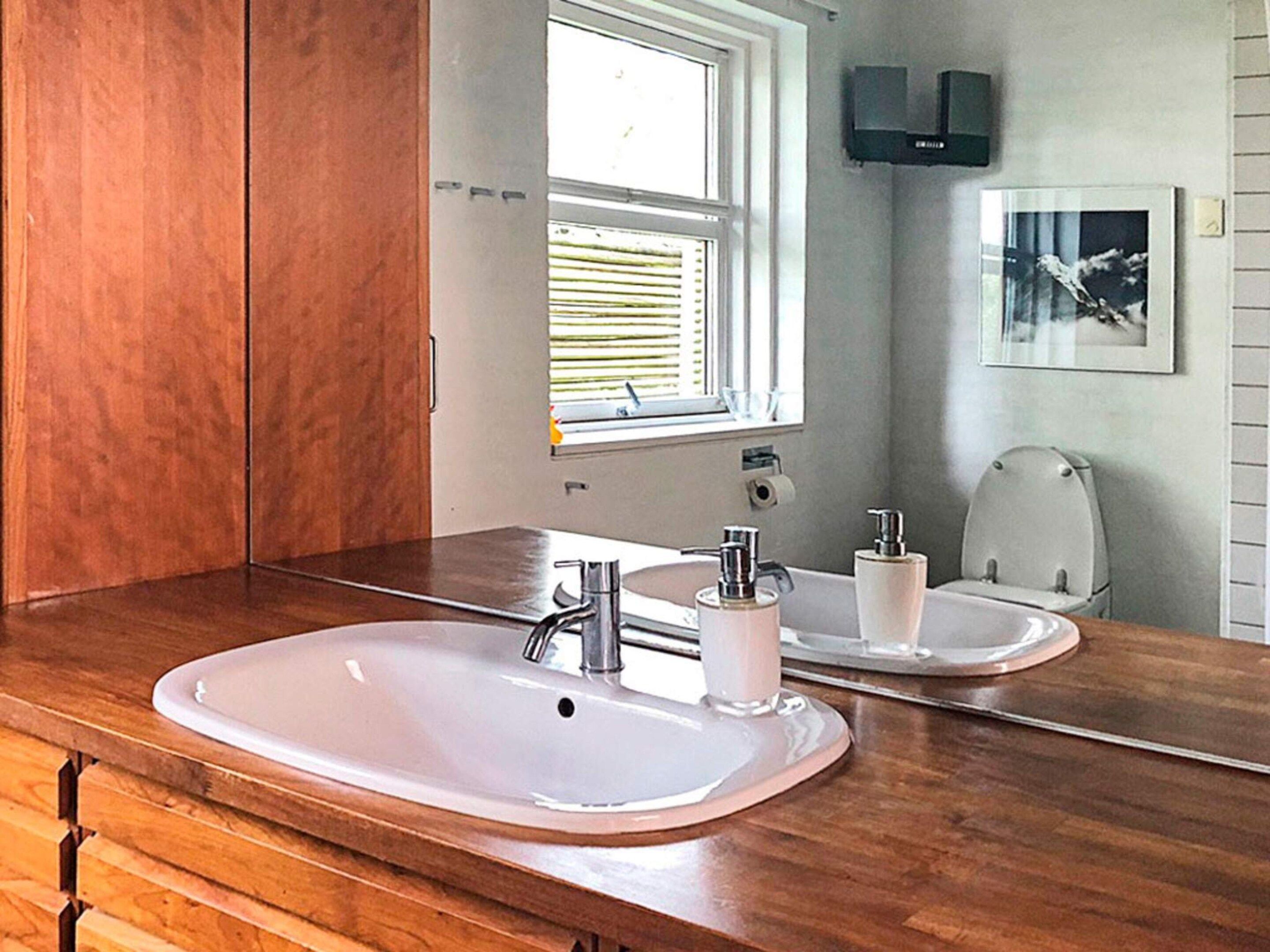 Un baño con tocador de madera, un espejo grande, un lavamanos y un inodoro.