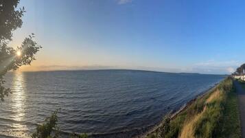 A coastal view with a clear sky, calm sea, and a grassy path along the shore.