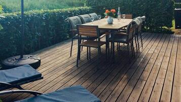 An outdoor deck with a wooden table and chairs, surrounded by greenery.