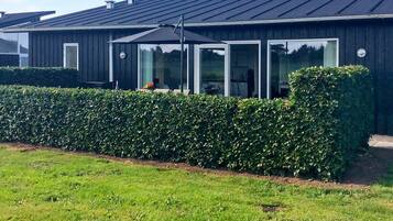 A modern building with a dark exterior, large windows, and a well-maintained hedge in front.