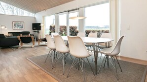 A modern living room with a dining area, large windows, and a view of the outdoors. - Holiday Home in Bogense (Bogense)