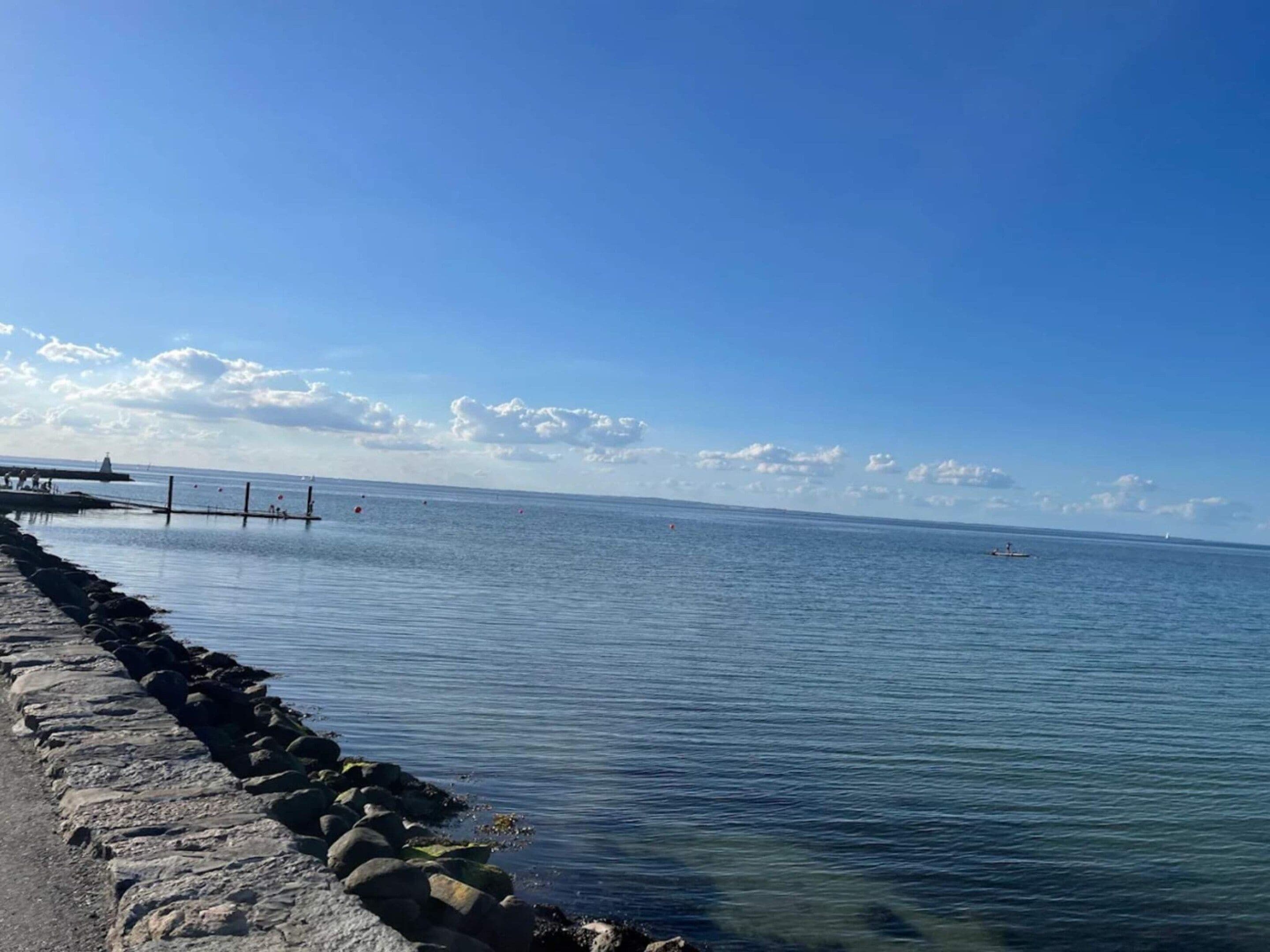 A calm sea with a stone breakwater and a pier extending into the water.