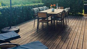 An outdoor deck with a wooden table and chairs, surrounded by greenery.