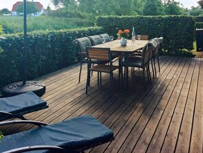 An outdoor deck with a wooden table and chairs, surrounded by greenery. - Holiday Home in Bogense (Bogense)