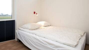 A single bed with white bedding in a room with a sloped ceiling and a window.