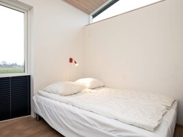 A single bed with white bedding in a room with a sloped ceiling and a window.