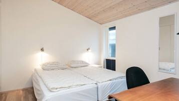 A small, single-room accommodation with a wooden ceiling, a bed with white bedding, a small table, and a chair.