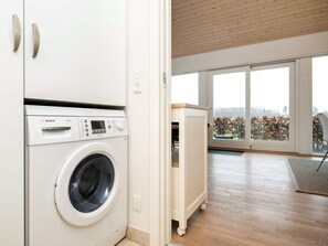 A modern laundry room with a Bosch washing machine, a wooden floor, and a view of a garden through large windows. - Holiday Home in Bogense (Bogense)