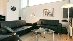 A modern living room with two black leather sofas, a glass coffee table, a floor lamp, a framed abstract painting, and a television. - Holiday Home in Bogense (Bogense)