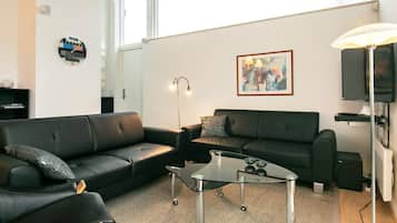 Un salon moderne avec deux canapés en cuir noir, une table basse en verre, un lampadaire, un tableau abstrait encadré et un téléviseur.