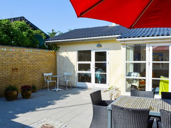 Une terrasse avec des meubles d’extérieur, un parasol rouge et un mur en briques.