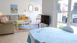 A cozy living room with a sofa, a small table, a TV, and a dining area with a table and chairs. - 4 Person Holiday Home in Blokhus (Blokhus)