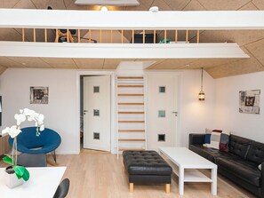 A modern loft apartment with a high ceiling, a staircase, a white sofa, a black leather ottoman, a white coffee table, and a blue chair. - Holiday Home in LÃ¸kken (Lokken)