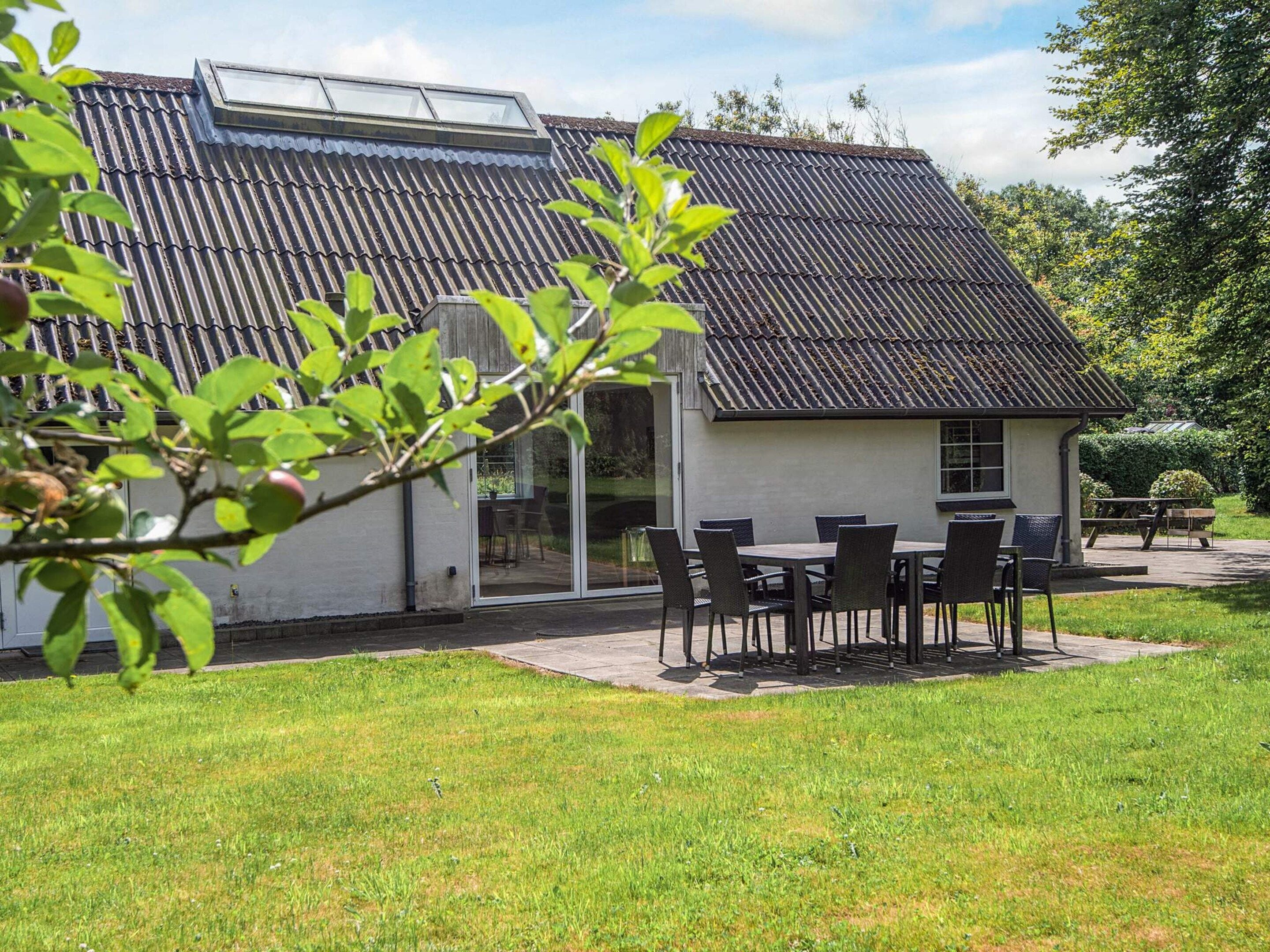 A house with a sloped roof, a patio with outdoor furniture, and a garden area.