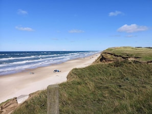 A beach with a grassy cliff, a sandy shore, and the ocean. - Holiday Home in LÃ¸kken (Lokken)