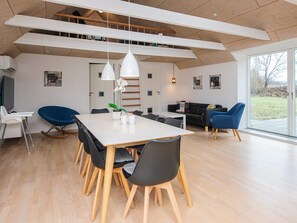A modern dining area with a white table, black chairs, and a blue rocking chair. - Holiday Home in LÃ¸kken (Lokken)