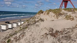 A beach with a red structure, white buildings, and the ocean. - Holiday Home in Blokhus (Blokhus)