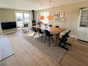 Un salon moderne avec une table à manger en bois, des chaises noires, une cheminée, un téléviseur et un coin cuisine avec des placards.