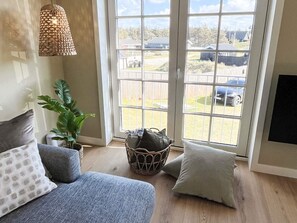 A room with a sofa, a potted plant, a woven basket, and a view through large windows.