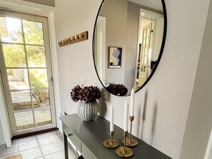 A hallway with a door leading to a garden, a mirror, a vase with flowers, and a console table with candles. - Holiday Home in Blokhus (Blokhus)