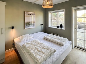 Une chambre à coucher avec un lit, une fenêtre, un tableau accroché au mur et un luminaire fixé au plafond.
