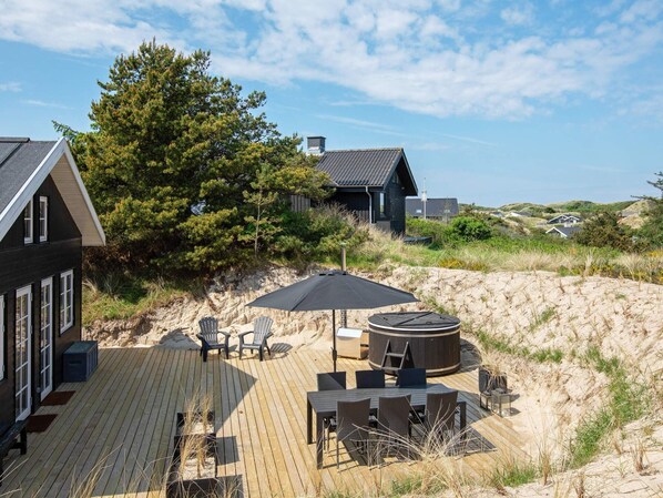 A wooden deck with outdoor furniture, a hot tub, and a view of a dune landscape.