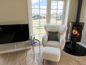 Un salon avec un téléviseur, un fauteuil confortable, une petite table avec une bougie et un poêle à bois.