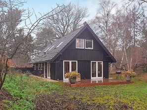 A dark wooden house with a gabled roof, white-framed windows, and a wooden deck. - Holiday Home in Solrød Strand (Solrod Strand)