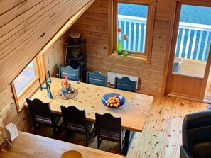 A wooden interior with a dining table, chairs, and a window overlooking the sea.