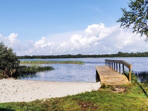 Un muelle de madera se adentra en un lago tranquilo con orilla cubierta de césped y cielo despejado.