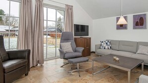 Uma sala de estar moderna com uma poltrona cinza, um sofá, uma mesa de centro e uma TV sobre um móvel de madeira.