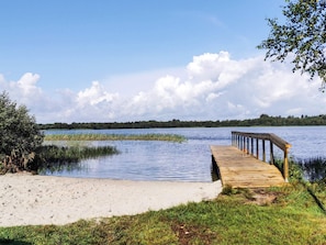 A wooden dock extending into a calm lake, surrounded by grassy areas and trees.