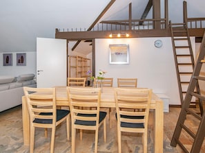 Un comedor con una mesa y sillas de madera, una escalera y vista de un paisaje urbano a través de un ventanal.