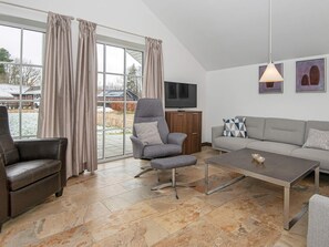 Una sala de estar moderna con un sofá gris, un sillón de cuero, un sillón gris con un cojín, una mesa de centro y un televisor sobre un mueble de madera.